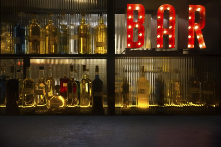 Vintage BAR sign with lights in the dark with bottles of alcohol and empty tabletop.